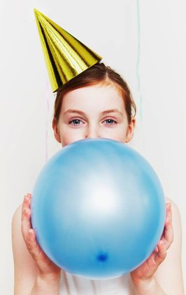 Girl in party hat, blowing up balloon